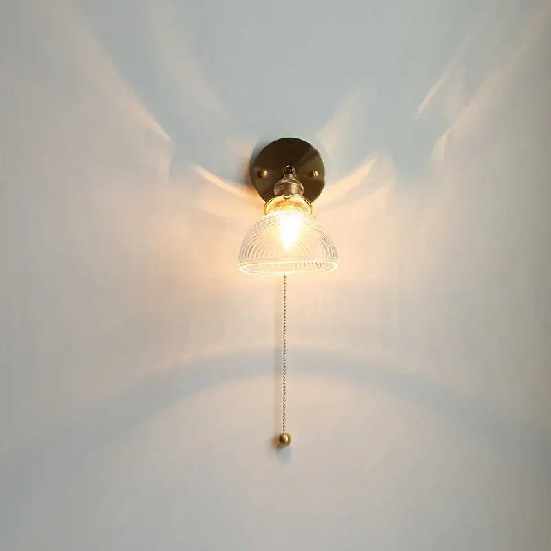 Vintage brass led wall light with warm-toned brass, clear ribbed glass shade, and ornate pull chain for bedroom sconce