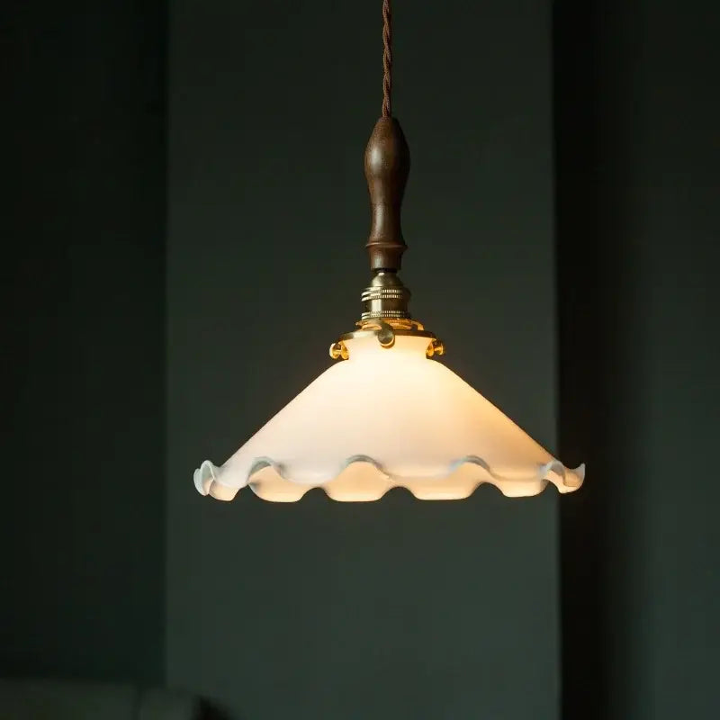 A warm frosted glass led pendant flower with scalloped edge and dark wood handle for vintage bedroom lighting