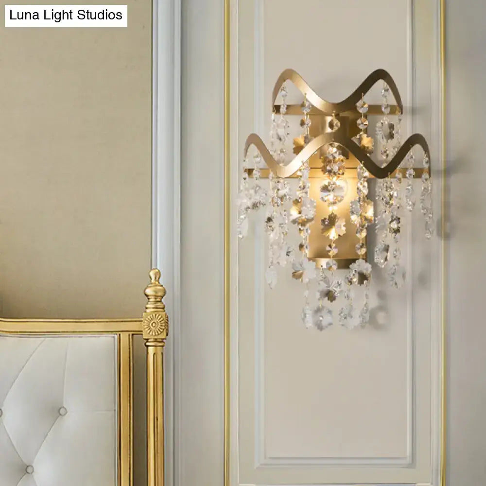 Vintage brass crystal wall sconce with direct wired power source, gold-toned wavy frame, bulb base, and dangling crystals