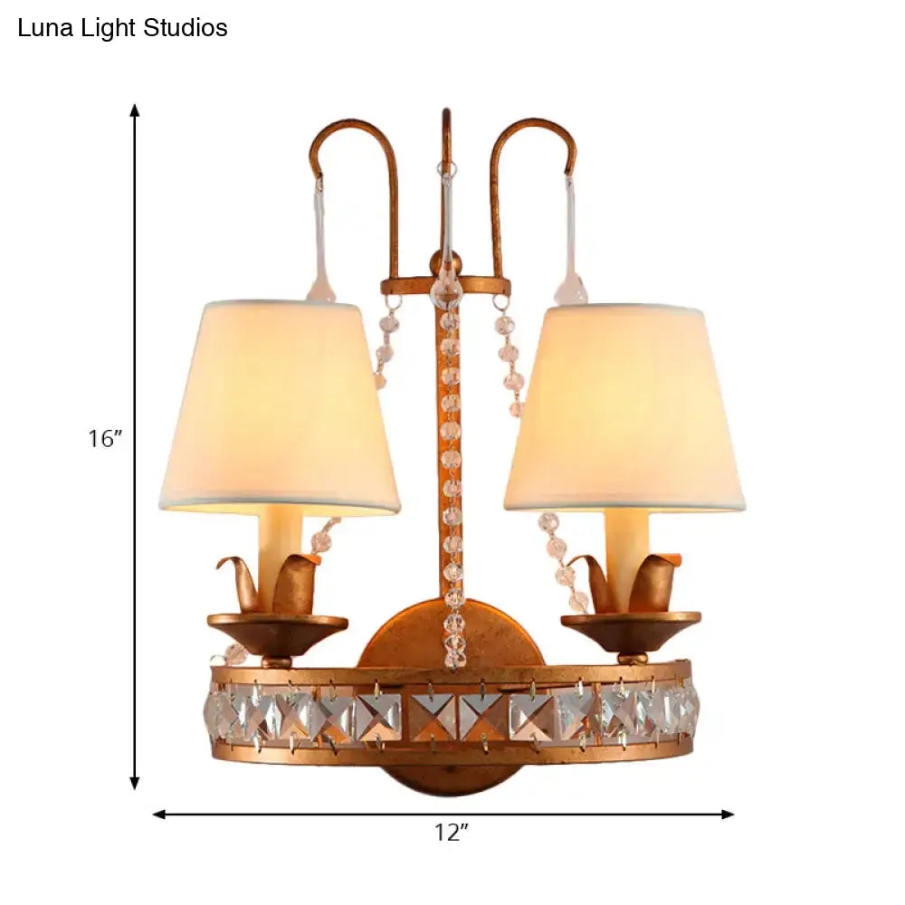 Antique brass finish two-light wall lamp with crystal accents and cream fabric shades for vintage bedroom sconces