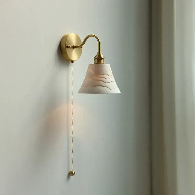 A delicate gold-finished wall sconce with off-white ceramic shade and pull chain for glass led bathroom decorbites use