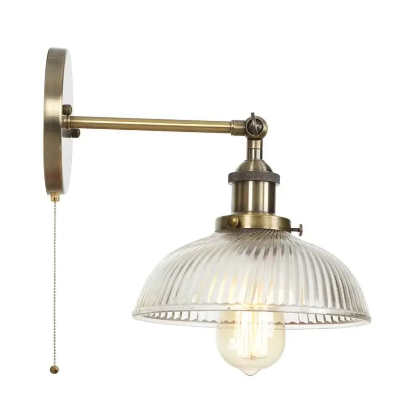 Vintage brass wall sconce with ribbed glass shade and pull chain switch featuring an exposed filament bulb