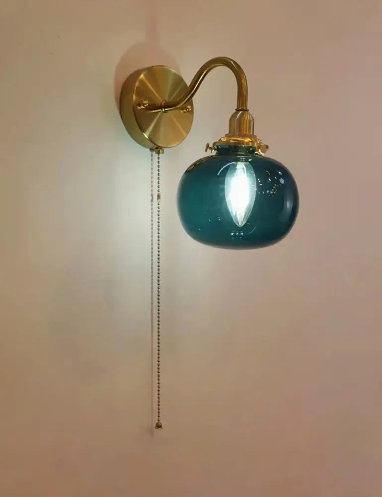 Teal glass globe wall sconce lamp with brass hardware and pull chain switch for vintage bedroom lighting