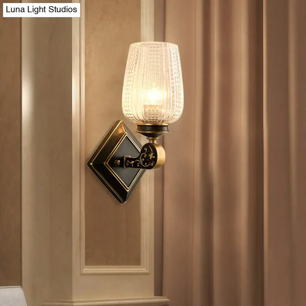 Vintage brass sconce featuring a clear textured glass shade and an ornate black metal base for living room lighting
