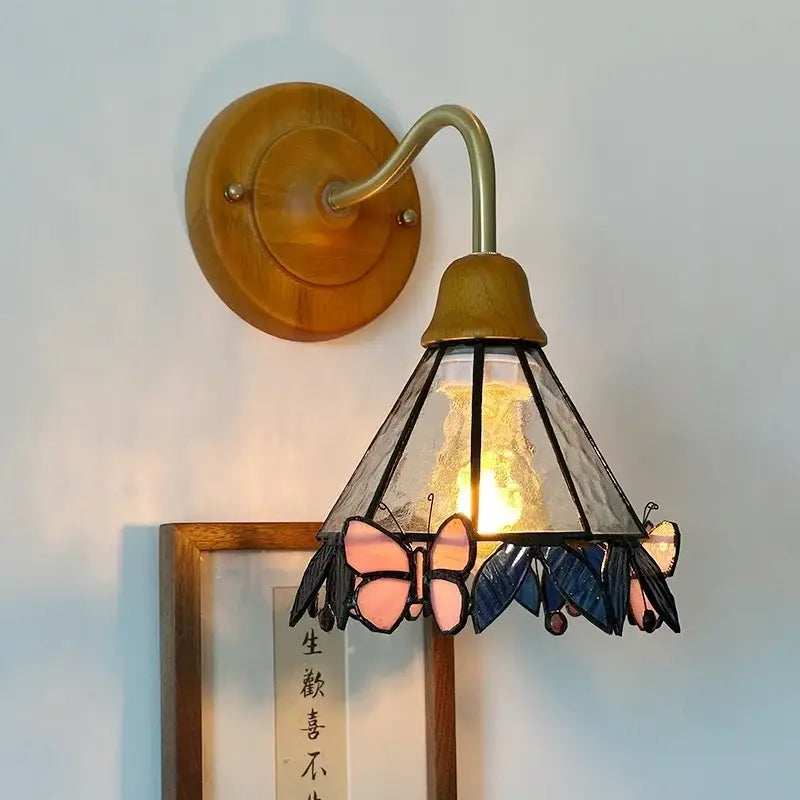 A warm-toned wall light with copper arm and decorbites butterfly glass shade in pink and blue for bedroom decor