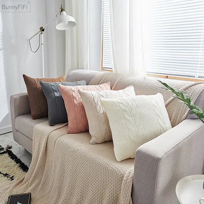 A cozy cream-colored decorbites cable knit throw blanket with textured cable knit double pattern draped over sofa