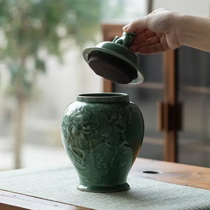 A jade-green celadon porcelain tea caddy with intricate dragon relief and matching lid lifted by hand as storage jar