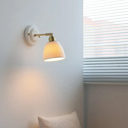 Vintage warm-toned ribbed ceramic and brass wall sconce light with pull chain mounted on white circular wall plate