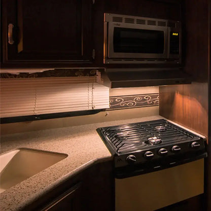 Black gas stove with four burners beneath a microwave featuring vintage clear glass led tubular bulb kitchen light
