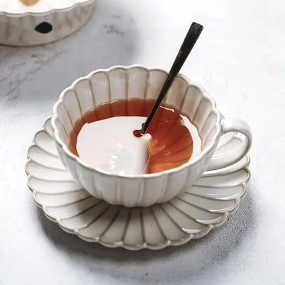 A delicate off-white ceramic teacup and saucer with scalloped design for a vintage cream dining table set