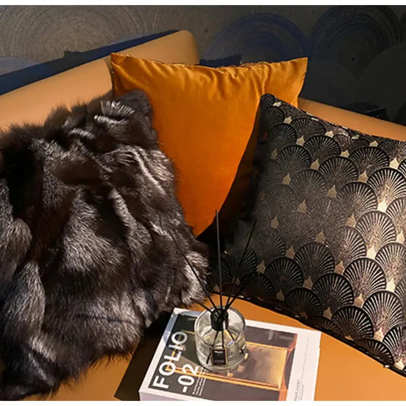 A clear glass diffuser with black reeds on an open magazine beside a vintage dark brown and black fox fur cushion cover
