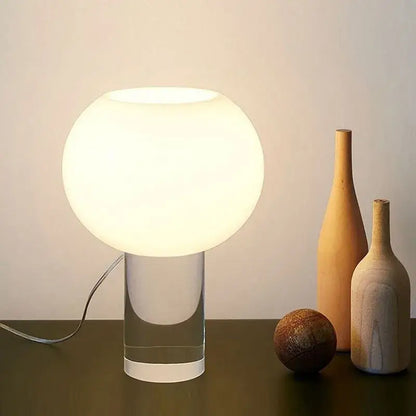 A sleek decorbites buds table lamp with frosted white glass shade and transparent acrylic base for warm bedroom glow