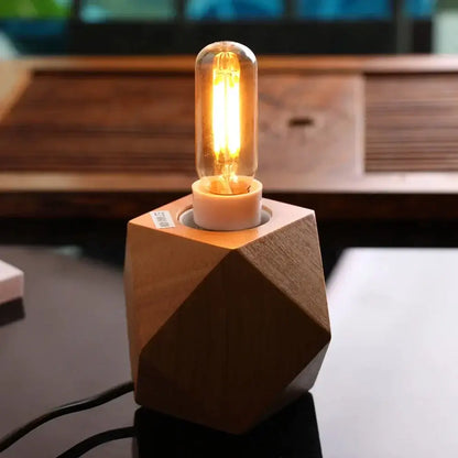 A warm glowing vintage gold tubular led bulb with clear glass on a geometric wooden base for dining room use