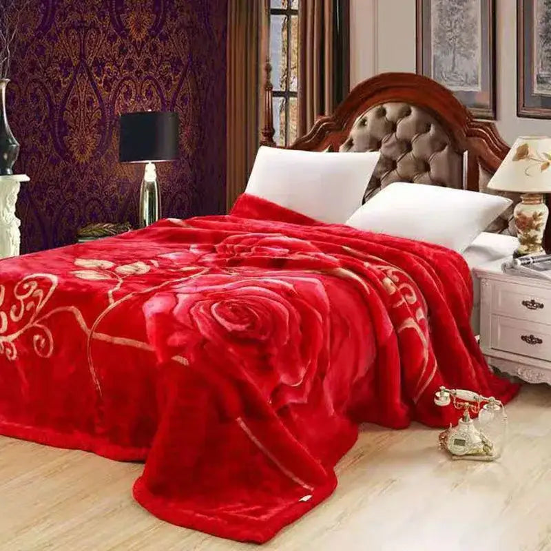 A plush red double layered raschel blanket with a large gold embroidered rose draped over a bed