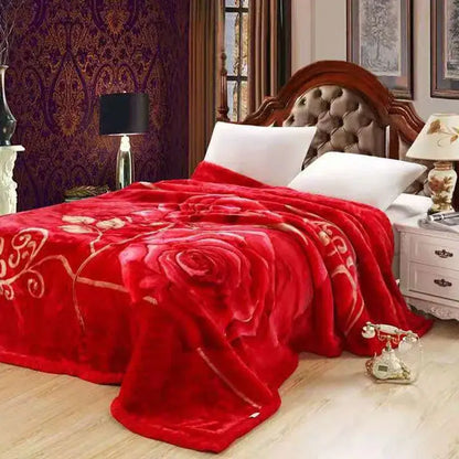 A plush red double layered raschel blanket with a large gold embroidered rose draped over a bed