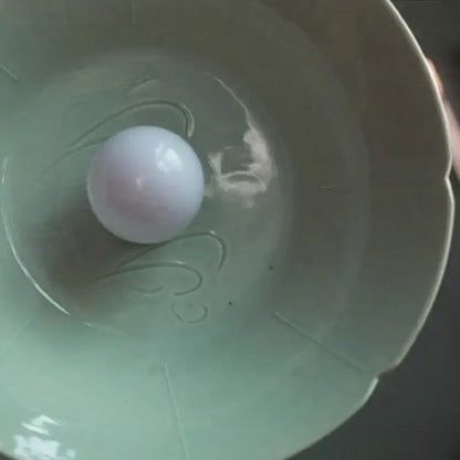 A smooth pale lavender sphere rests in a shallow celadon green ceramic bowl of a vintage green ceramic pendant light