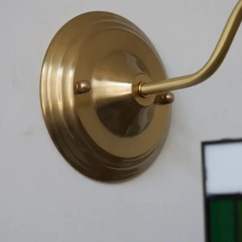 Brass wall sconce with a circular base and curved arm featuring vintage green glass led star stair light design