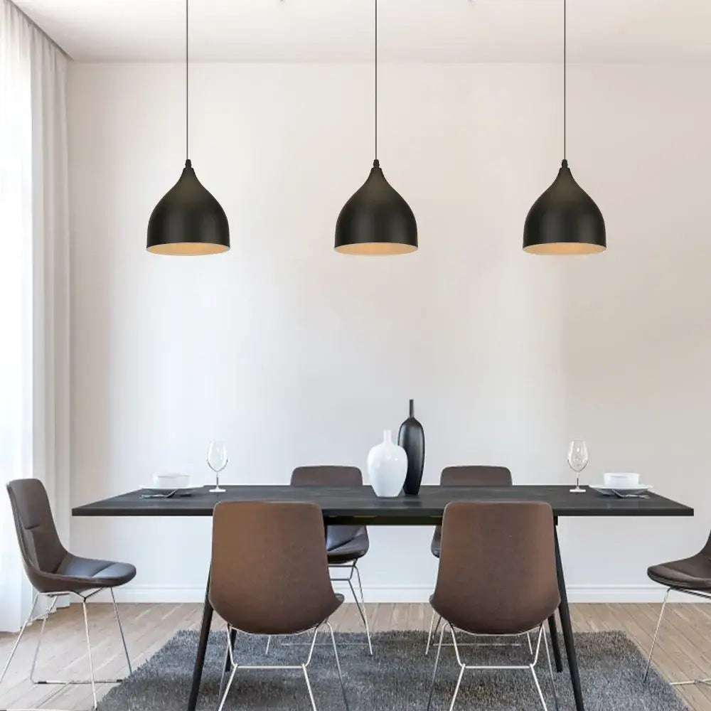 Three sleek iron black pendant lights with gold interiors hang above a modern dining table by decorbites