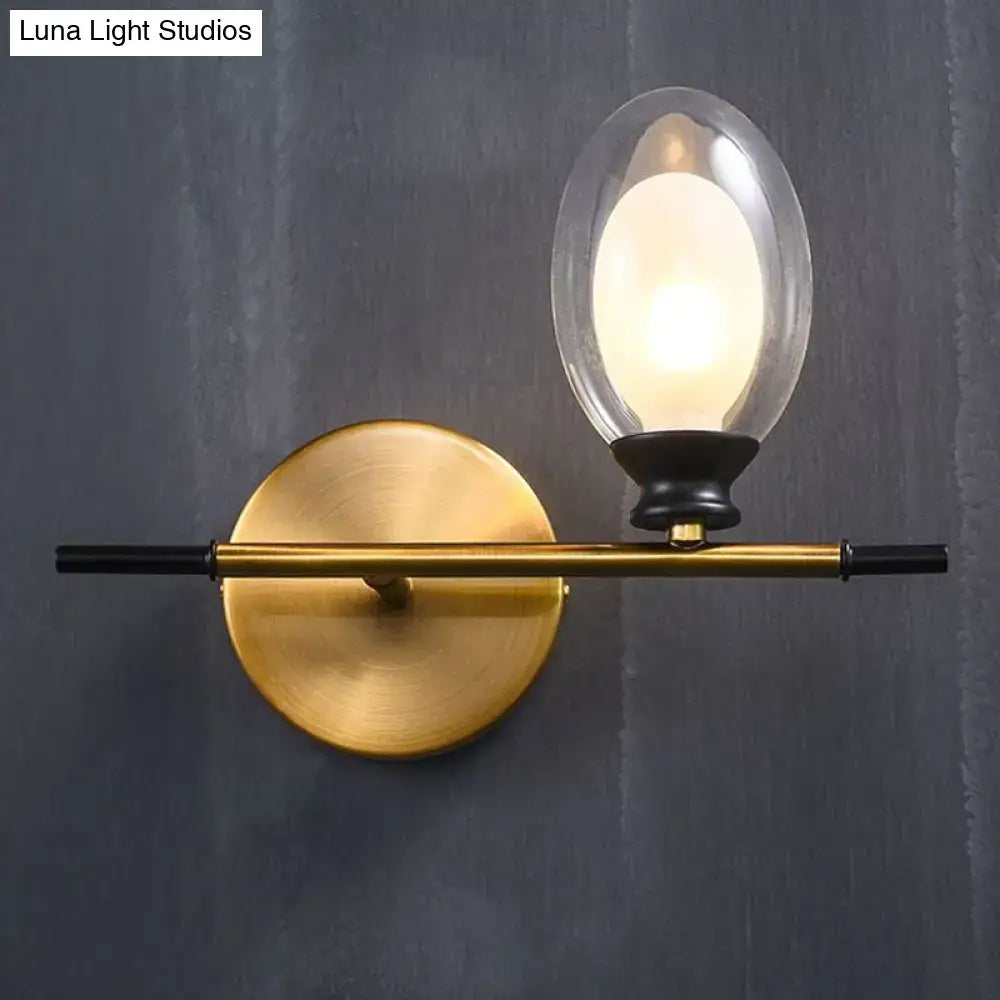 Vintage oval wall sconce in gold-toned brass with black rod and oval glass shade for bedroom lighting