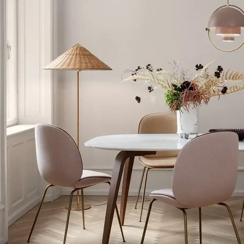 Blush pink upholstered dining chairs with slender gold-tone legs paired with a vintage gubi rattan shade floor lamp decorbites