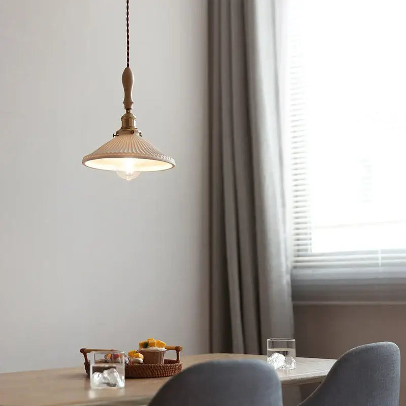 A warm-toned vintage ceramic led pendant light with ribbed shade and brass accents hanging from braided cord