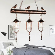 Copper-toned DecorBites vintage metal island lighting with three caged shade bulbs and decorative bird element rust finish