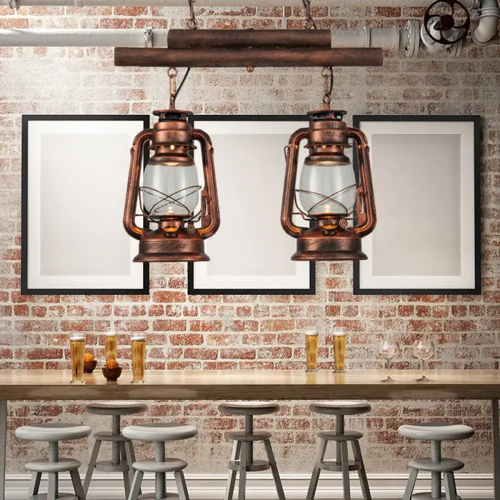 Two vintage-style copper lanterns with clear glass and intricate metalwork hang from rustic wooden beam in kitchen fixture