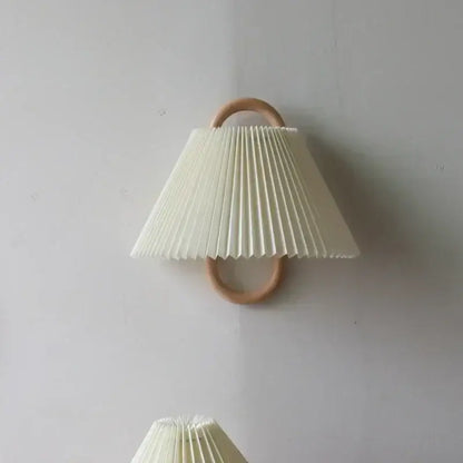 Off-white pleated fabric shade wall lamp mounted on a light beech wood ring for bedroom use