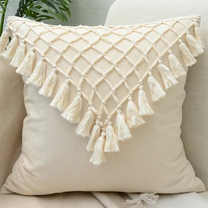 Cream-colored tufted cushion cover with diamond-patterned macrame top and tassels for wabi-sabi living room decor