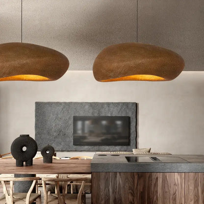 Two warm-toned handmade polystyrene indoor pendant lights with textured earthy brown finish hang above dining area decorbites