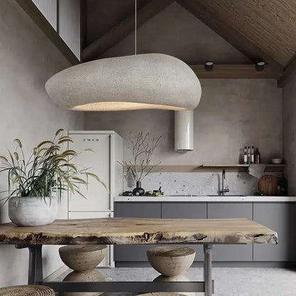 A textured light gray decorbites handmade polystyrene indoor pendant lamp with a cloud-like shape above a dining table