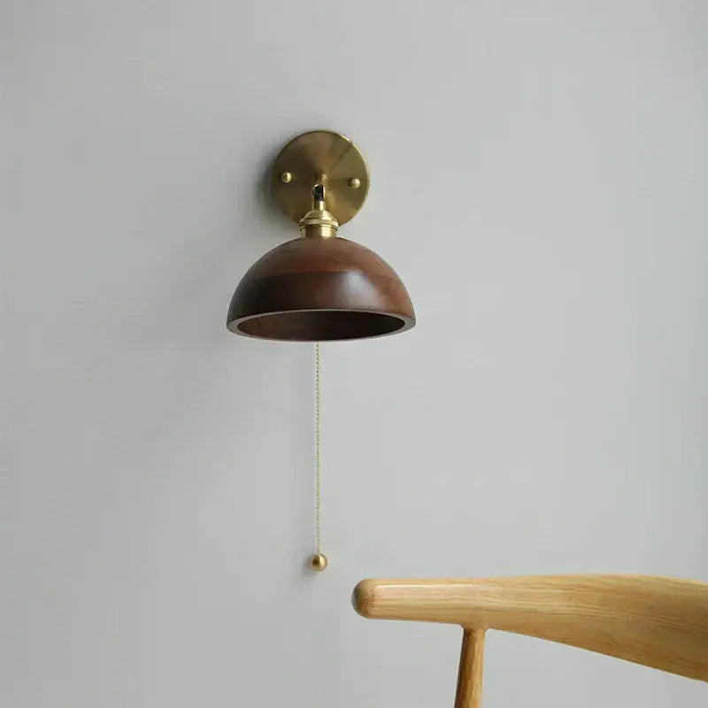 Walnut and brass wall sconce with dome-shaped dark wood shade and pull chain switch for bedroom lighting