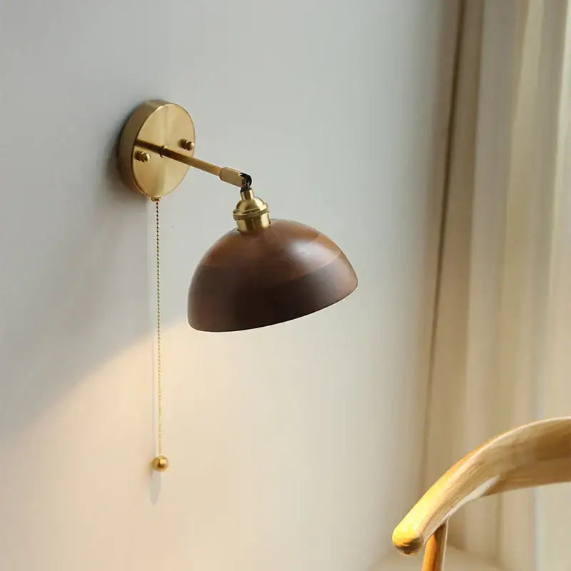 Walnut and brass wall sconce with polished wooden dome shade and adjustable arm featuring a pull chain switch