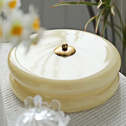 Cream-colored ceramic round lidded container with gold knob next to warm chrome double layer glass led ceiling light