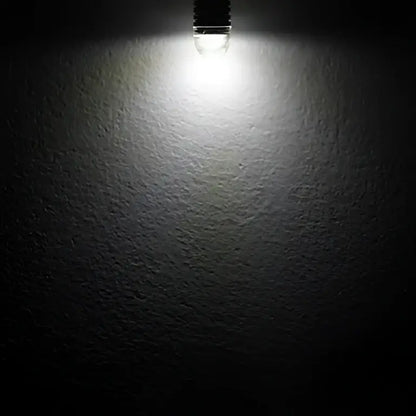 A bright white warm white frosted decorbites g4 led bulb against a textured dark gray wall for home lighting