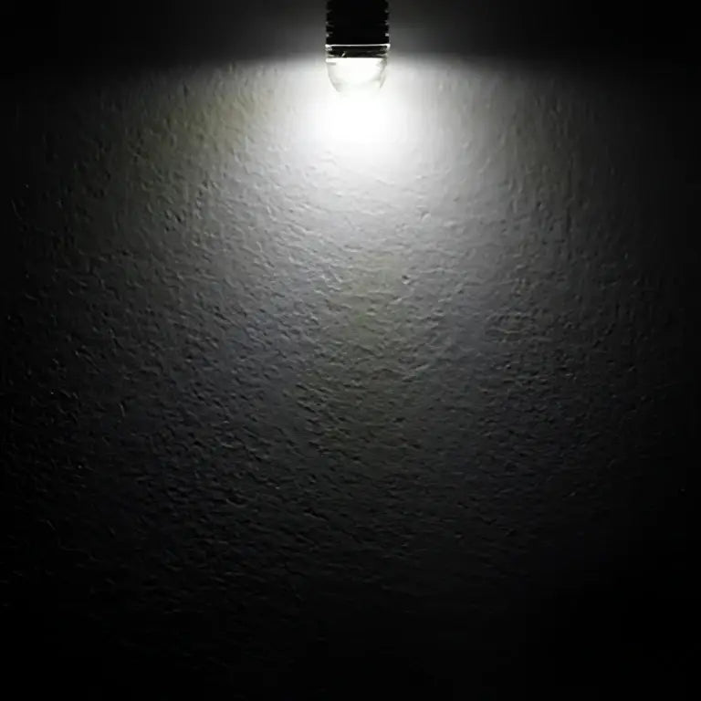 A bright white warm white frosted decorbites g4 led bulb against a textured dark gray wall for home lighting