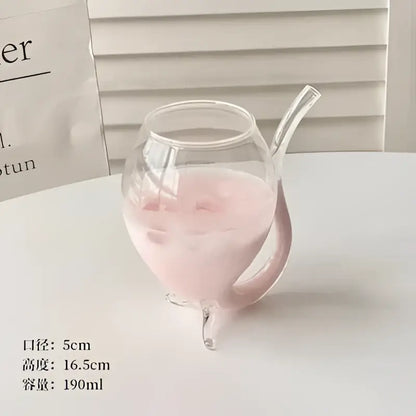 A clear glass vampire cocktail glass cup with curved handle and three feet filled with pink liquid for dining decor