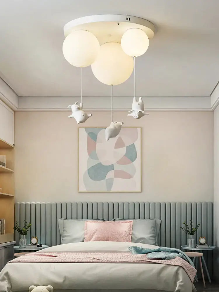 White ceiling light with three spherical bulbs and dangling flying pig resin figurines for bedroom use