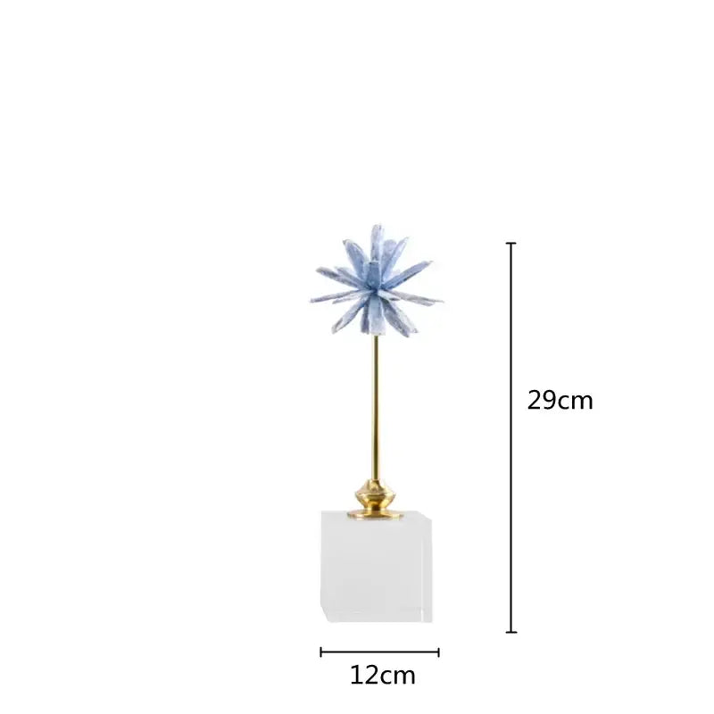 A light blue crystalline flower home decor figurine on a gold stem resting on a clear acrylic marble base