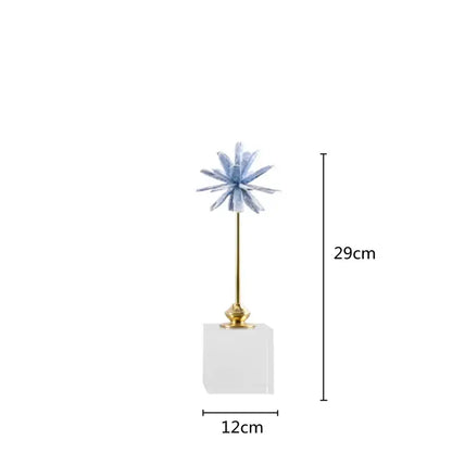 A light blue crystalline flower home decor figurine on a gold stem resting on a clear acrylic marble base