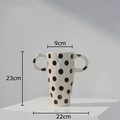 A tall cream-colored ceramic vase with black polka dot pattern and two looped handles for living room decor