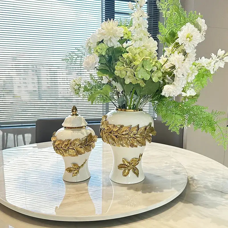 White and gold leaves ceramic flower vase with decorbites golden leaves embellishments holding white flowers and greenery