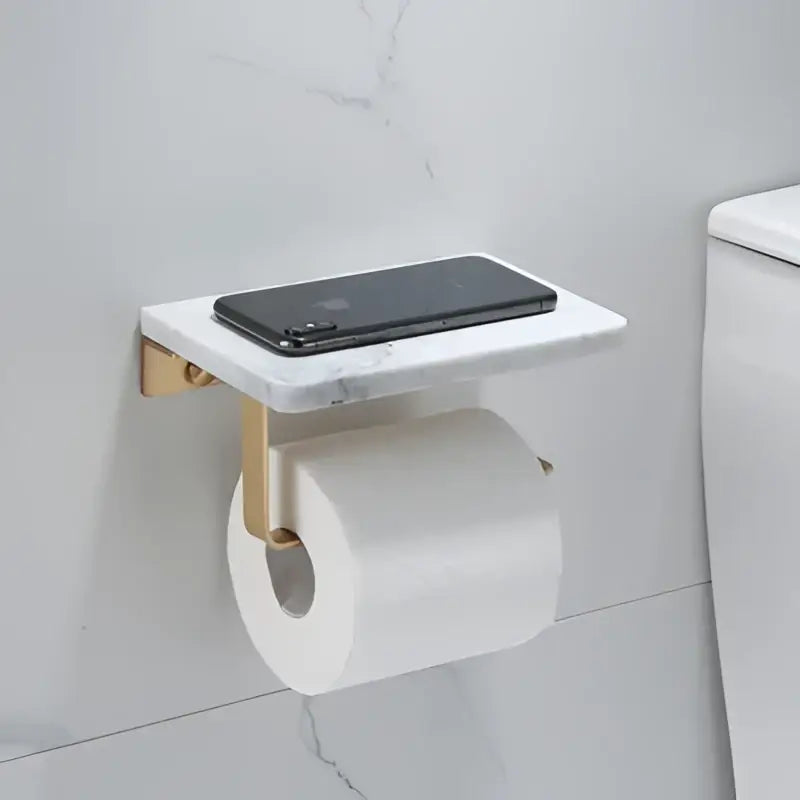 White and gold marble toilet paper holder with gold marble metal brackets and matching bathroom shelf holding smartphone