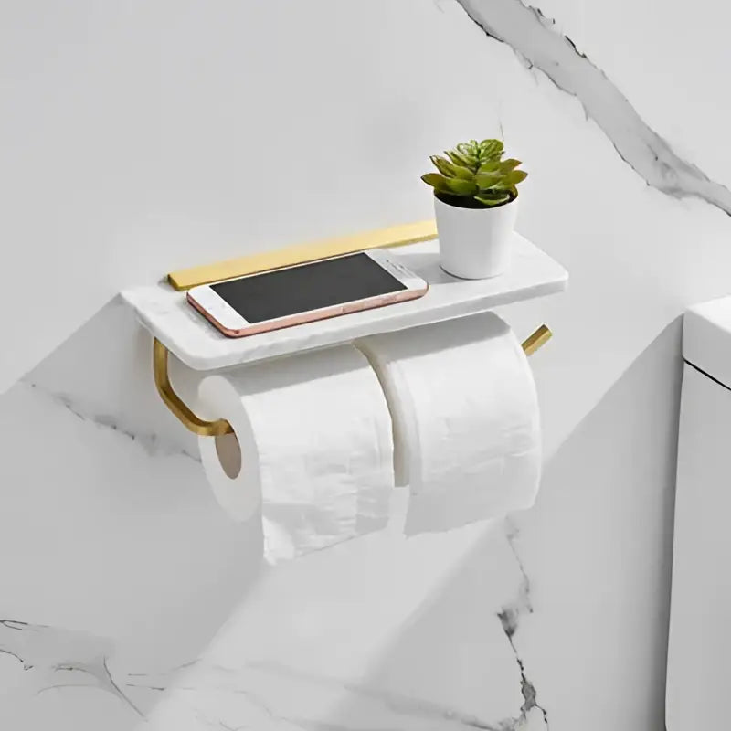 White and gold marble toilet paper holder with gold marble arms and shelf holding a smartphone and small plant decorbites gold marble