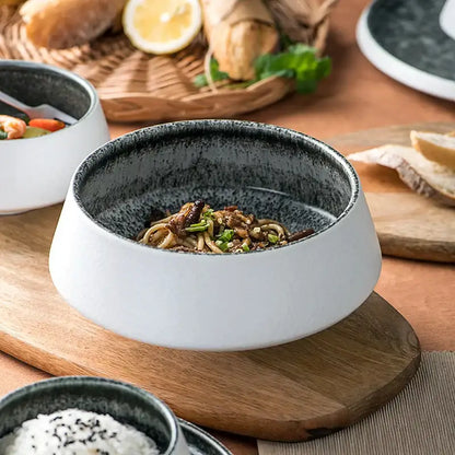 A modern white and grey ceramic bowl with ice cracked glaze and speckled black interior filled with noodles