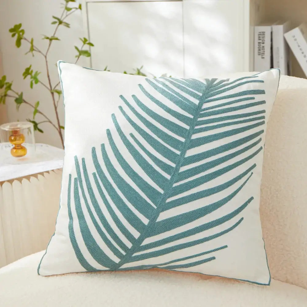 White cushion pillow cover with teal embroidered leaf design for living room decor featuring embroidered leaf pillow detail