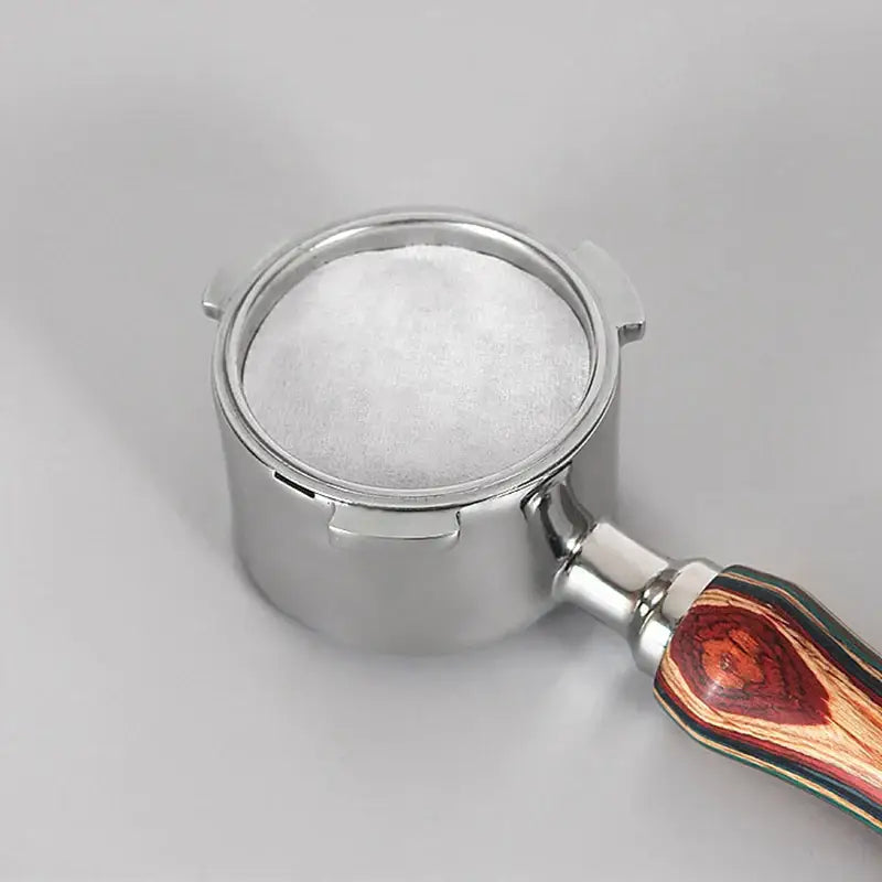 A stainless steel espresso portafilter with a colorful wood-grain handle holding finely ground white coffee filter papers