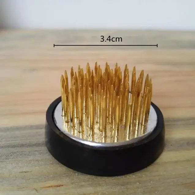 Golden sewing needles arranged upright in a black base with silver circle beside white cobblestone deformation ceramic vase decorbites cobblestone deformation