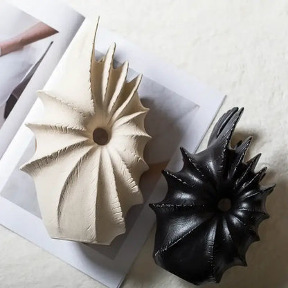 Two conch shape ceramic vases in matte off-white and glossy black for artificial flower arrangements on magazine