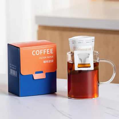 White disposable paper coffee filter bags filled with dark roasted grounds in a clear glass mug for pour over use